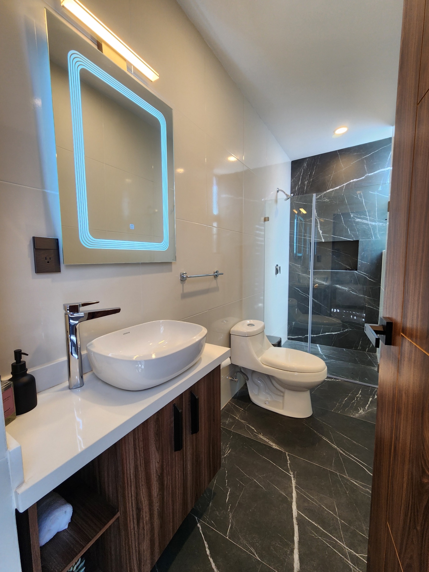 Baño con regadera de mármol, cancel de cristal templado, espejo retroiluminado y mueble en madera
