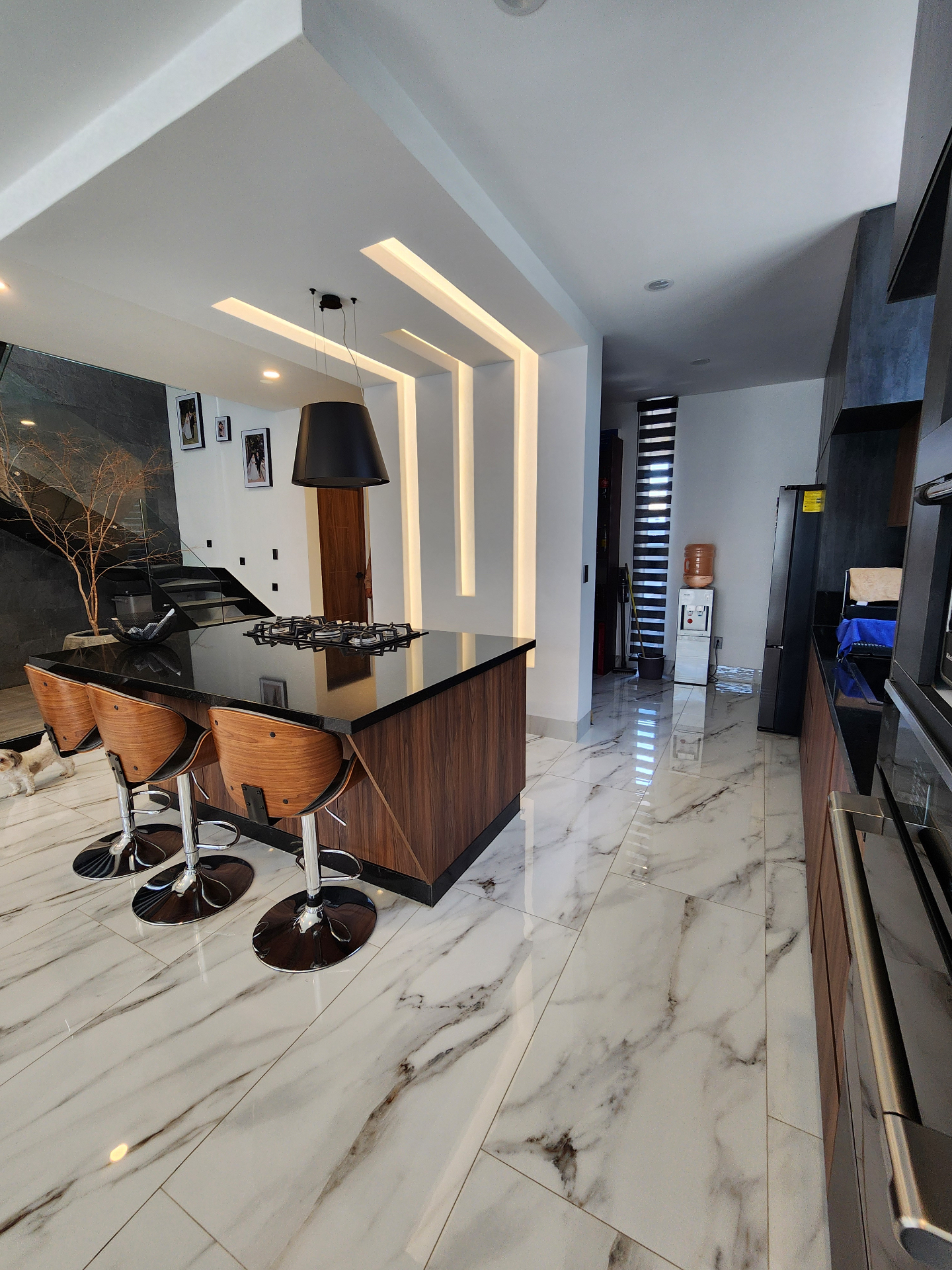 Cocina con isla central, cubierta oscura, luminarias lineales y equipamiento completo