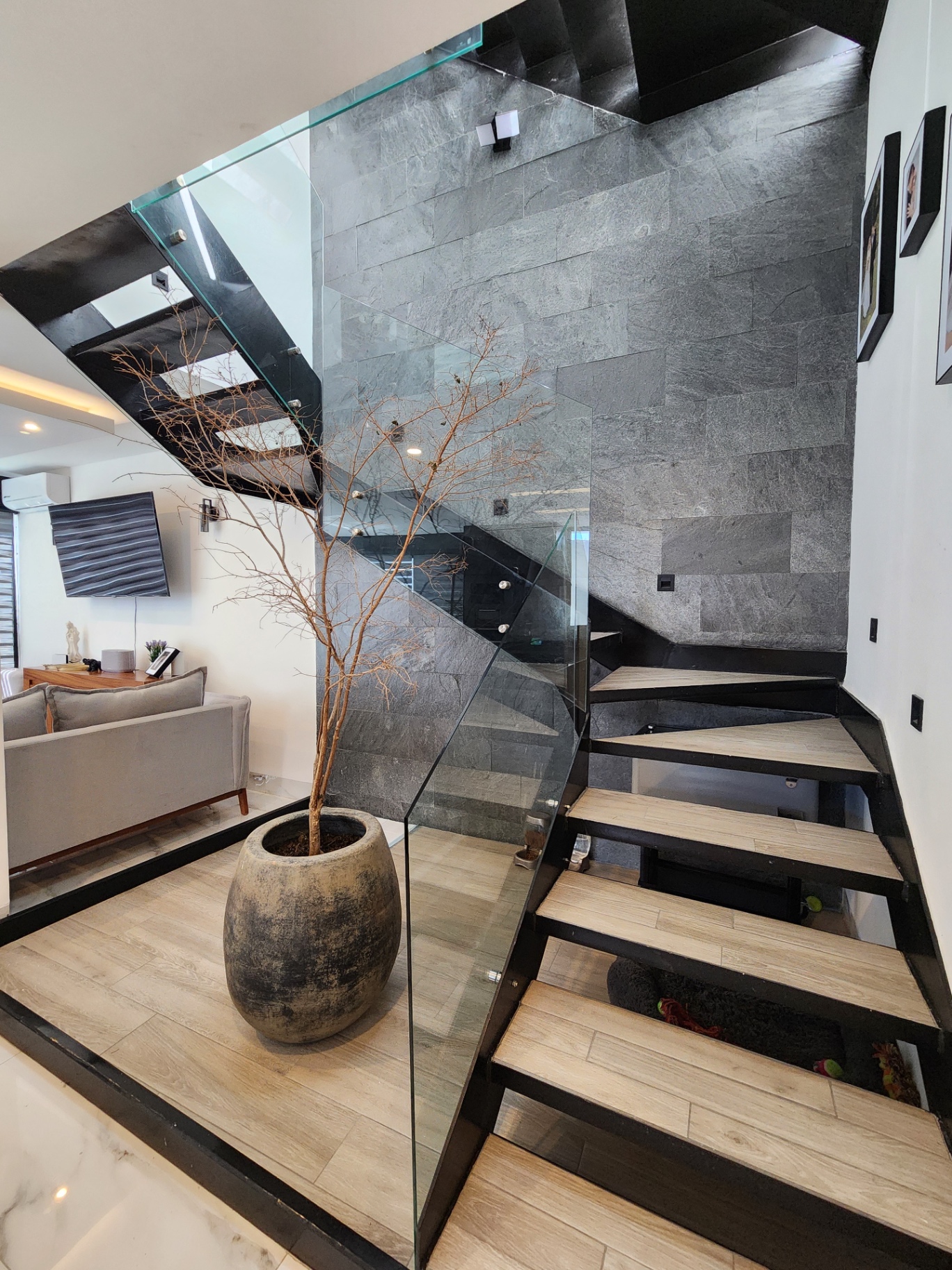 Escalera de estructura metálica negra con peldaños de madera, barandal de cristal templado y maceta decorativa