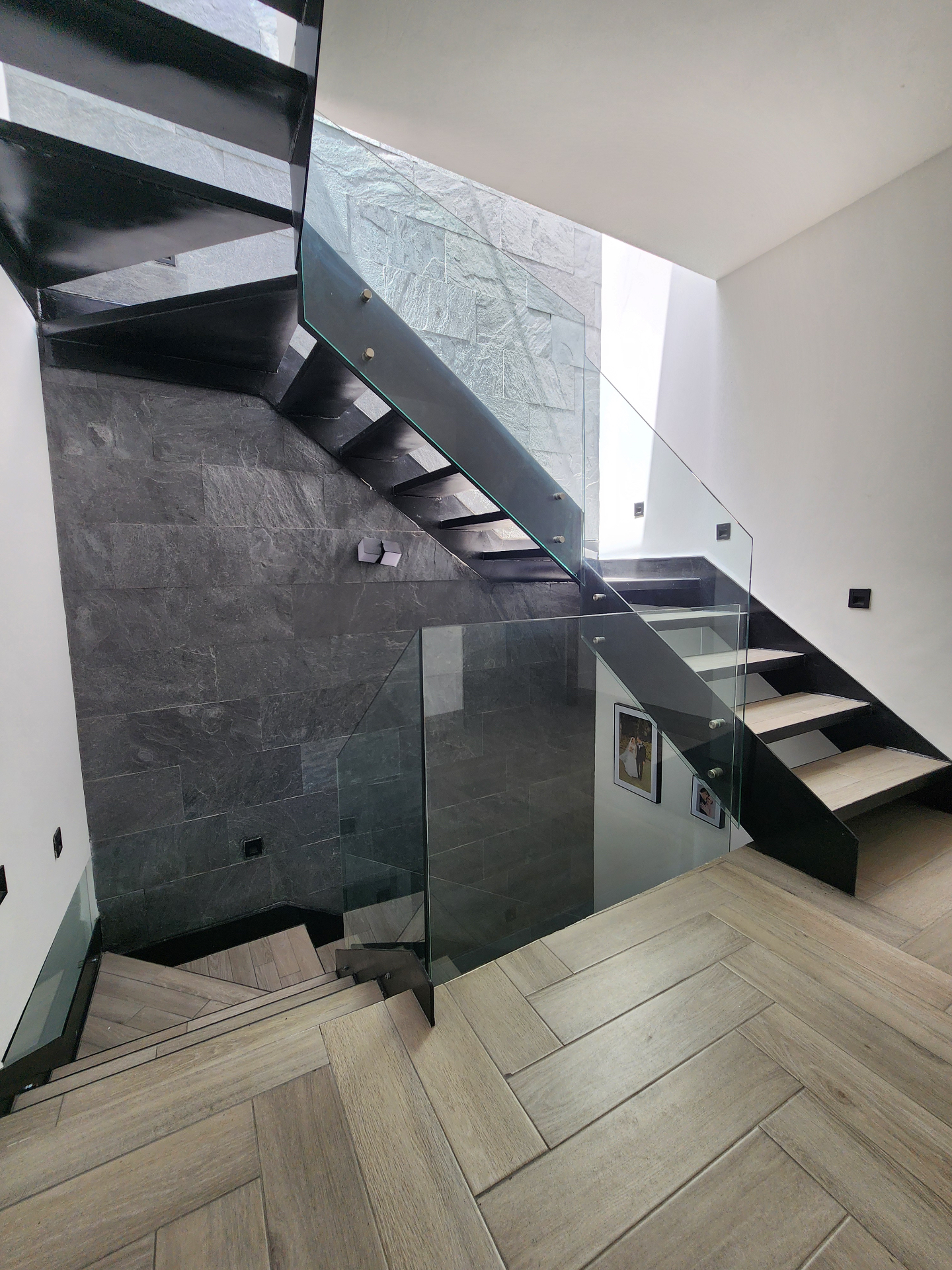 Doble altura con muro de piedra natural gris, escalera flotante y piso de madera en espiga