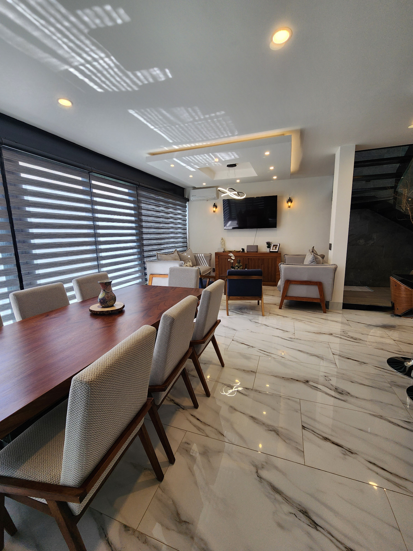 Sala y comedor con grandes ventanales, acabados en madera y piso porcelánico tipo mármol